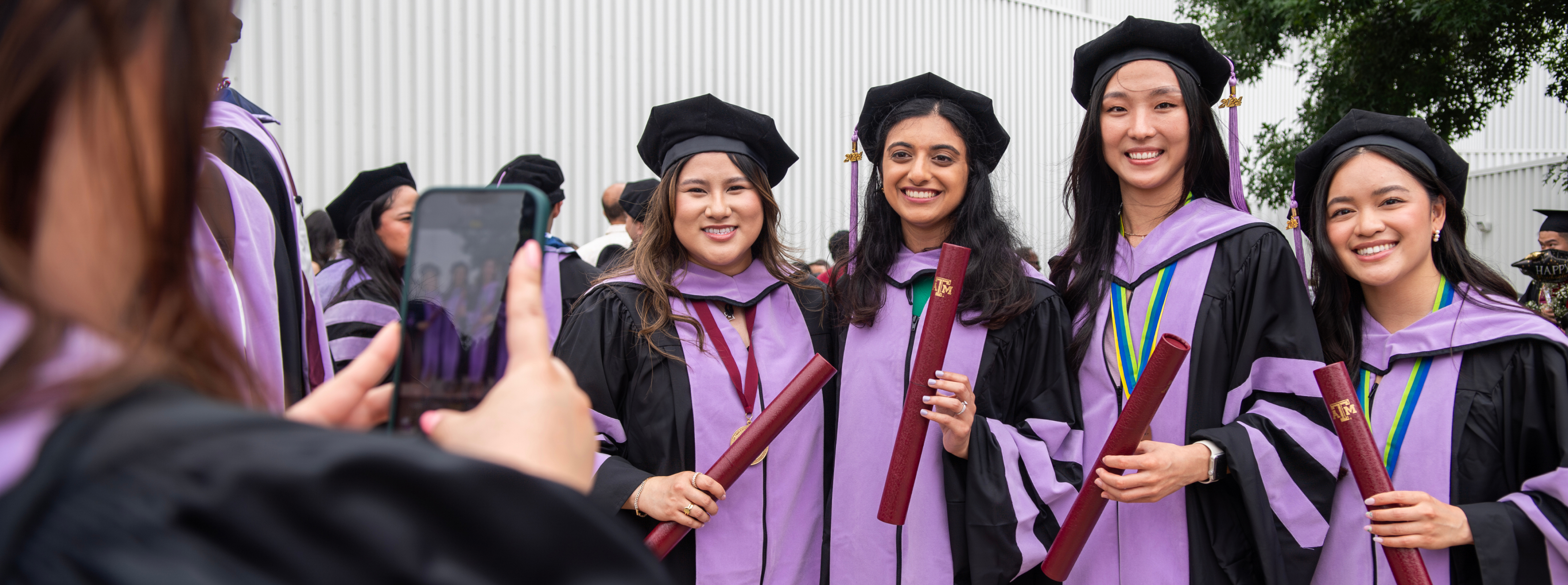 Four dental school graduates smile while being photographed at commencement.