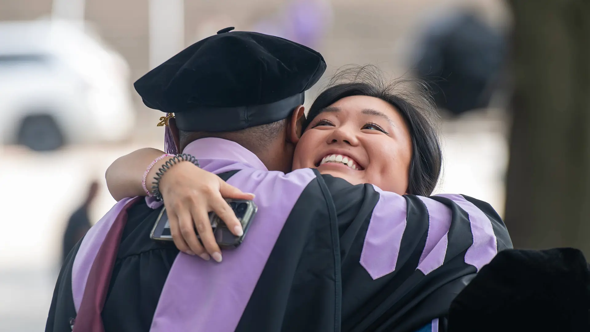 A woman dental school graduate in regalia hugging a classmate.
