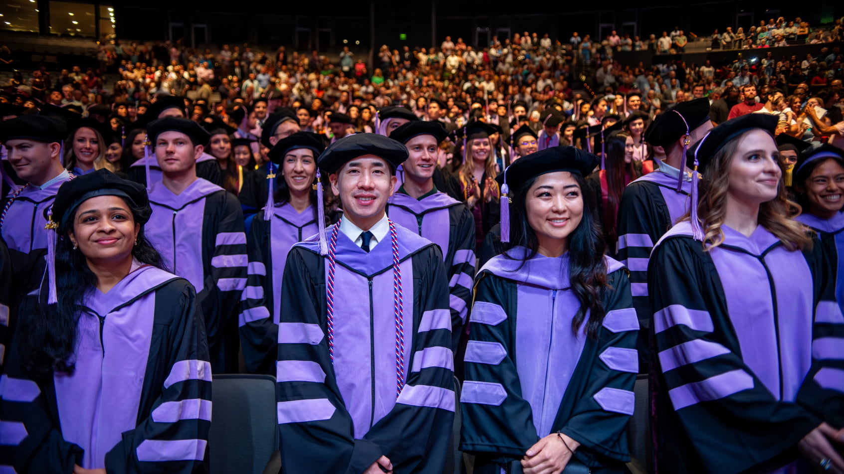 Dental school graduates in caps and gowns smile during a commencement ceremony.