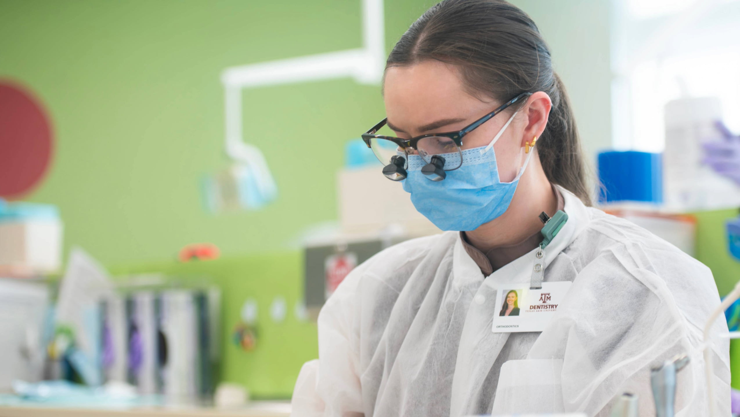 A dental student in a white coat and mask focuses on a clinical task.