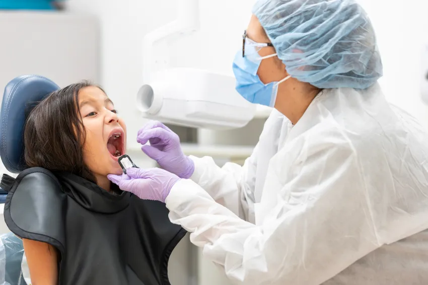 A dental provider examines a young child's open mouth during a dental appointment