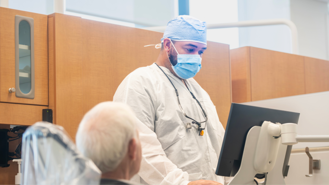 Dentist in mask at a computer speaking with a patient.