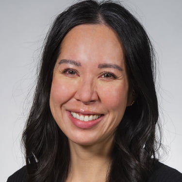 Professional headshot of Victoria Woo, DDS, smiling warmly with dark hair framing her face against a neutral gray background.