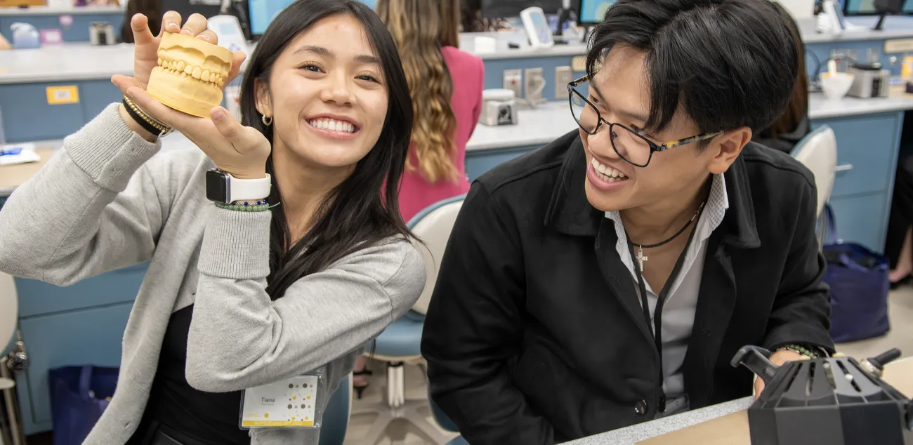 Two smiling dental students examine a dental model in a lab setting.