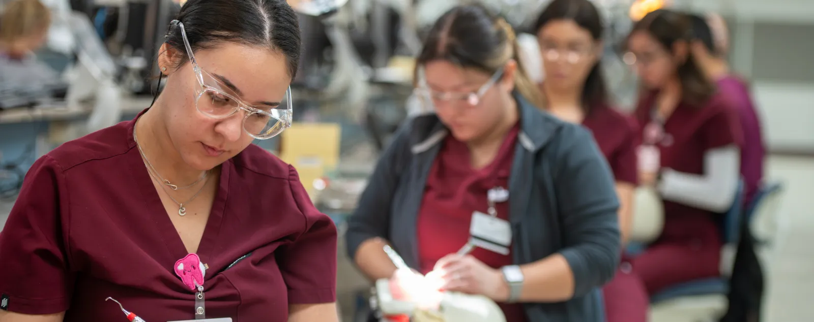 A row of dental students in scrubs practice clinical skills in a dental simulation lab