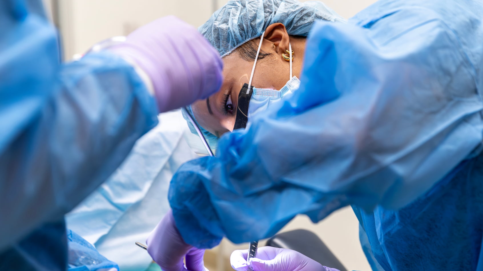 Two dental providers in full surgical attire perform a procedure together in a clinical setting.