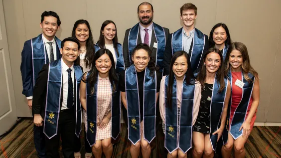 Group portrait of eleven smiling graduates and award recipients wearing formal attire and blue satin stoles